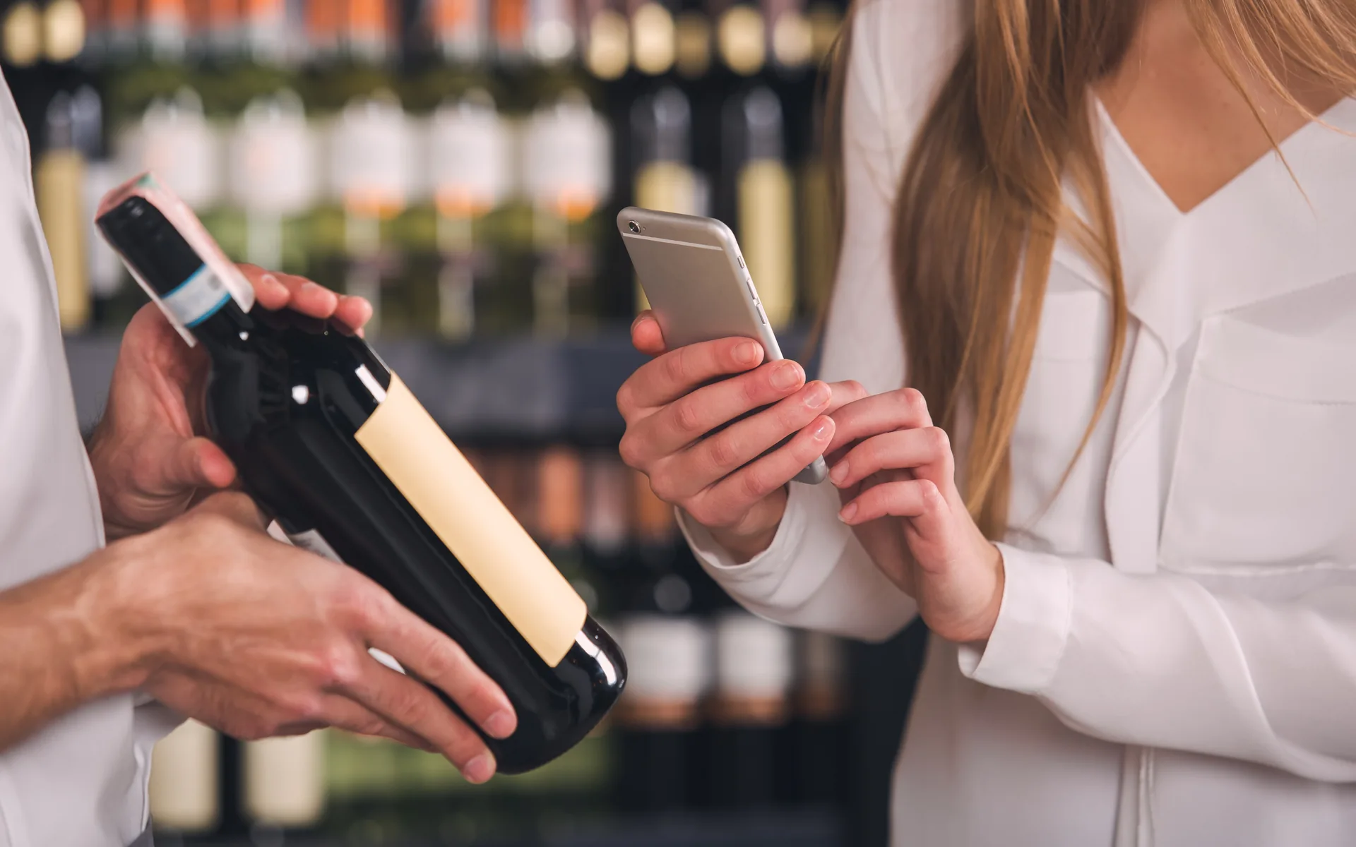 A buyer checking a bottle label against a phone in a retail aisle